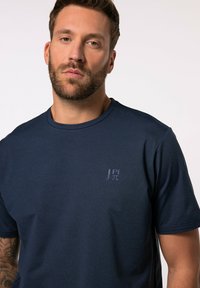 T-shirt blu navy in morbido tessuto con collo rotondo, caratterizzato da un logo discreto sul petto e maniche corte, texture liscia.