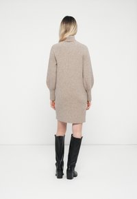 Abito maglione in beige chiaro con collo alto e maniche lunghe, abbinato a stivali neri con tacco al ginocchio. Tessuto liscio e aderente.