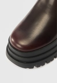 Βουργουνδί δερμάτινη μπότες μέχρι τον αστράγαλο με στρογγυλή μύτη, υφασμάτινη μαύρη καουτσούκ σόλα και σχεδιασμό επιπέδ�ου με στρώσεις που διαθέτει αυλάκια για πρόσφυση.