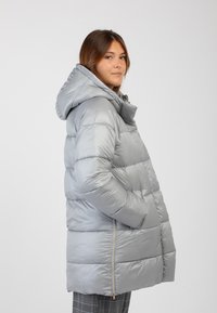Giacca a vento argentata con cappuccio, presenta un design trapuntato, tasche con zip, texture brillante e una silhouette ampia.