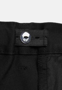 Fascia in tessuto nero con un bottone trasparente e un piccolo anello cucito. Materiale texturizzato con una finitura liscia e bordi puliti.