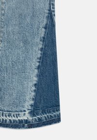 Falda de denim con un diseño a bloques de color que presenta paneles en tonos de azul claro y oscuro, un dobladillo deshilachado y una textura suave.