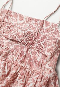 Robe sans manches fleurie rose avec fines bretelles et taille froncée sur un fond en tissu clair.