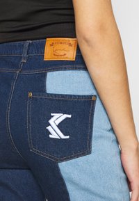 Jeans de mezclilla con un cuerpo principal azul oscuro y paneles laterales azul claro. Etiqueta de cuero en la parte posterior de la cintura, logo bordado en el bolsillo.