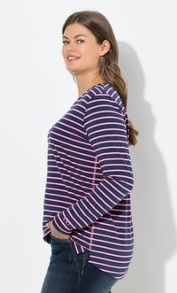 Sininen ja vaaleanpunainen raitapaitapaita, jossa on pitkät hihat ja pyöreä kaula-aukko, sivutaskut ja kaareva helma, pidetty tummien farkkujen päällä. Suora kangas.