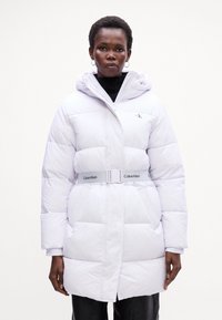 Biely puffový kabát s kapucňou, s prešívaným dizajnom, opaskom v páse a logom Calvin Klein na hrudi a opasku. Hladká textúra.