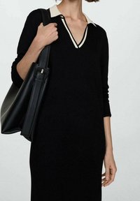 Abito maglione nero con scollatura a V e dettagli di colletto color crema. Maniche lunghe e vestibilità comoda. Porta una borsa in pelle nera.