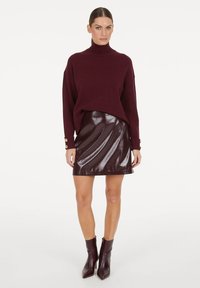Burgunderfarbener Strick-Turtleneck-Pullover, lockere Passform, kombiniert mit einem glänzenden burgunderfarbenen Minirock. Schwarze Ankle Boots mit spitzer Zehenpartie runden den Look ab.