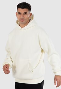 Weißer Hoodie aus weichem Stoff, mit einer geräumigen Fronttasche und Kapuze mit Kordelzug. Gerippte Bündchen und Saum sorgen für Textur.