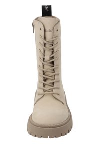 Botas beige con cordones, con un acabado liso y mate, punta redonda, suela texturizada y una pestaña en la parte posterior para facilitar su uso.