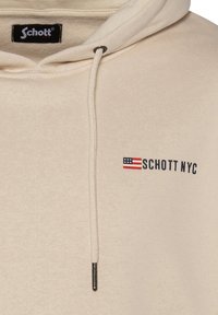 Beige Kapuzenpullover mit Kordelzug, ausgestattet mit einem schwarzen Etikett und einem kleinen rot, weiß und blau gestreiften Flaggenmuster neben dem Aufdruck "SCHOTT NYC".
