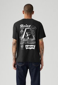 Sort bomulds t-shirt med forskellige hvide grafikker, herunder "Relax," et stort bogstav "A," og "Levi’s," med en afslappet pasform og korte ærmer.
