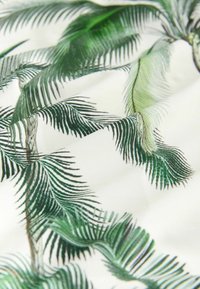 Tissu arborant un motif de feuilles de palmier vertes sur fond blanc, avec des textures détaillées et des nuances variées de vert dans le feuillage.