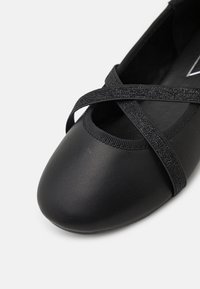 Czarne baletki z okrągłym noskiem, wykonane z gładkiego materiału. Posiadają krzyżujące się elastyczne paski oraz teksturowane wykończenie wokół otwarcia.