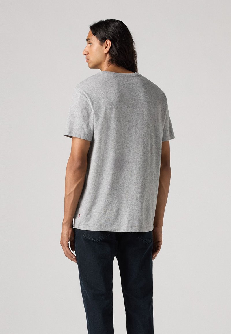 Camiseta gris de manga corta hecha de algodón con cuello redondo. La parte trasera presenta una textura suave y una pequeña etiqueta de la marca cerca del dobladillo.