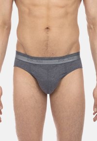 Mann trägt graue Low-Rise-Slips mit elastischem Bund, der mit "HOM" beschriftet ist, und zeigt den Bauch und die Oberschenkel.