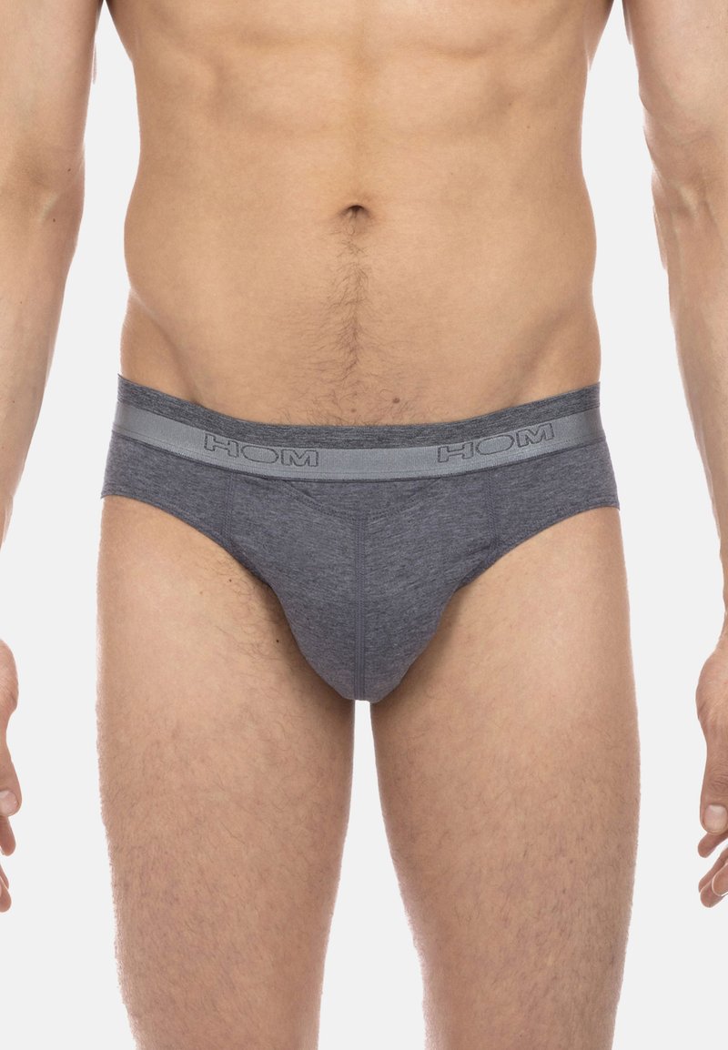 Mann trägt graue Low-Rise-Slips mit elastischem Bund, der mit "HOM" beschriftet ist, und zeigt den Bauch und die Oberschenkel.