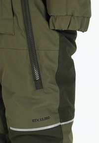 Wasserabweisende olivgrüne Jacke mit einem schwarzen Reißverschluss, verstellbarem Bund, STX 15.000 Etikett und reflektierenden Akzenten am Saum.