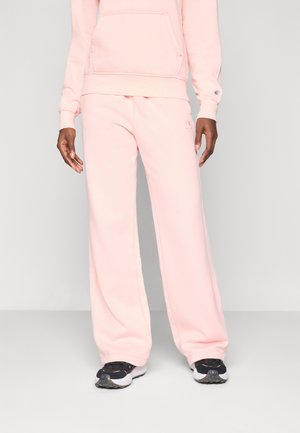 Roze katoenen hoodie met een voorzak en bijpassende roze wijde sweatpants. Zwart-witte sportieve schoenen maken de outfit compleet.
