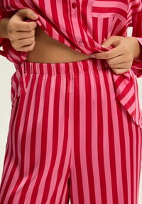 Różowo-czerwony, paskowany komplet satynowej piżamy z guzikiem i spodniami na elastycznej talii, o gładkiej fakturze i luźnym kroju.