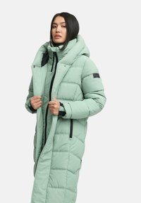 Lange pufferjas in licht mintgroen, met een gewatteerd ontwerp, grote capuchon, dubbele ritssluiting en zwarte accentdetails.