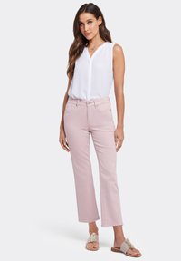 Jeans rectos de color rosa claro con cierre de botón, combinados con una blusa sin mangas blanca. Las sandalias tienen acentos florales.