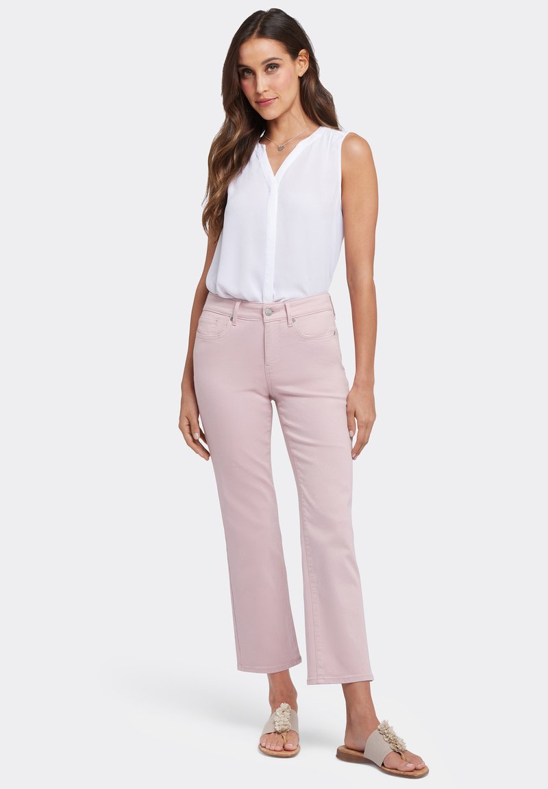 Jeans rectos de color rosa claro con cierre de botón, combinados con una blusa sin mangas blanca. Las sandalias tienen acentos florales.
