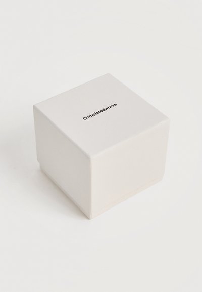 Λευκό τετράγωνο κουτί με την επιγραφή "Completedworks" σε μαύρο, τοποθετημένη στο κέντρο της πάνω επιφάνειας, σε απλό λευκό φόντο.