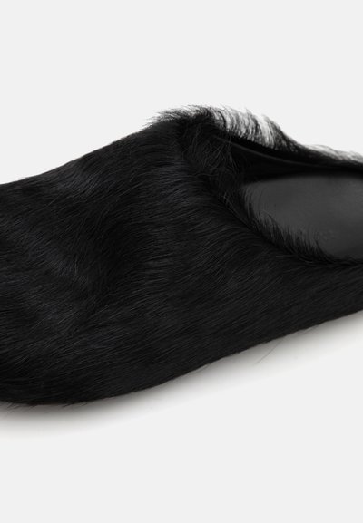 Pantofii negri, tip slip-on, cu o textură asemănătoare blănii și un design cu vârful rotunjit. Talpa este netedă, iar marginea superioară are detalii moi, pufoase.