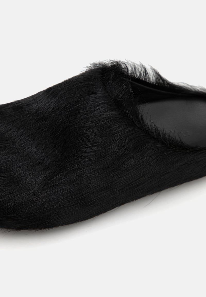 Scarpa nera slip-on con una texture simile alla pelliccia e una punta arrotondata. La suola è liscia, e il bordo superiore presenta dettagli morbidi e piumati.