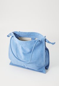 Sac à main en daim bleu avec une texture douce, ouverture en haut, fermeture à cordon, et un intérieur spacieux. Présente des bords arrondis et un design minimaliste.