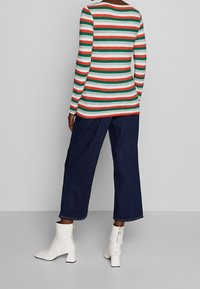 Langarmhemd mit roten, grünen und weißen horizontalen Streifen; kombiniert mit weiten, dunklen Jeanshosen und weißen Ankle Boots mit Reißverschlüssen.