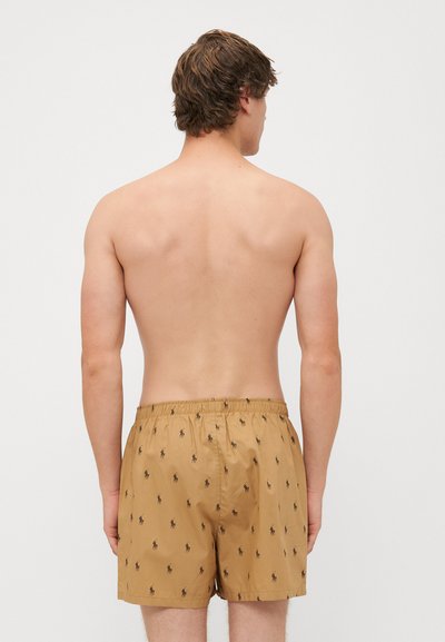 Shorts de baie maro cu un model subtil repetitiv negru, talie elastică și un material ușor, neted. Vedere din spate.