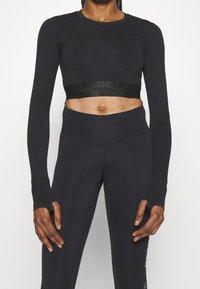Czarny krótki top z długim rękawem o dopasowanym kroju, z paskiem z logo na wysokości talii. Do tego wysokie czarne legginsy z wysokim stanem.