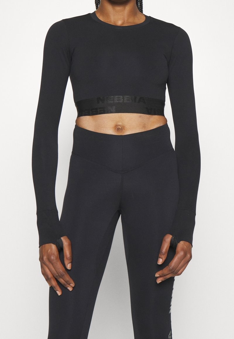 Czarny krótki top z długim rękawem o dopasowanym kroju, z paskiem z logo na wysokości talii. Do tego wysokie czarne legginsy z wysokim stanem.