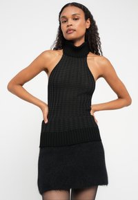 Top halter tricotado preto com uma gola alta canelada e padrão texturizado, apresentando um corpete ajustado e uma bainha canelada.