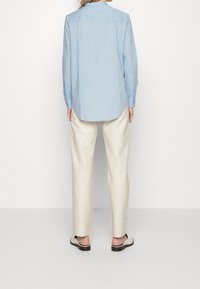 Ljusblå, långärmad skjorta med rundad nederkant, i kombination med krämfärgade byxor. Skjortan har knappade manschetter och en mjuk, slät textur.