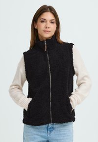 Zwarte fleece vest met hoge kraag, ritssluiting aan de voorkant en twee zijzakken. Mouwen in crèmekleur bieden contrast. Casual pasvorm.