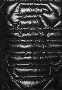Černá nadýchaná bunda zblízka, se šitým vzorem s geometrickými tvary, lesklým povrchem a kontrastními stehy.