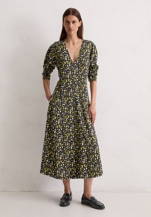 Lang zwart dress met geel en witte abstracte patroon, diepe V-hals, driekwart mouwen, aansluitend lijfje en uitlopende rok. Gekocht met zwarte instappers.