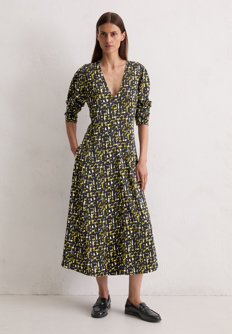 Lang zwart dress met geel en witte abstracte patroon, diepe V-hals, driekwart mouwen, aansluitend lijfje en uitlopende rok. Gekocht met zwarte instappers.