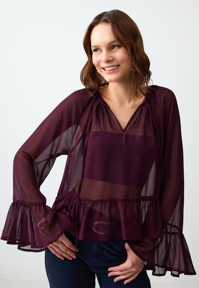 Camicia trasparente borgogna con scollo a V, maniche lunghe, polsini arricciati e orlo a peplum. Presenta accenti sottili sulle maniche.