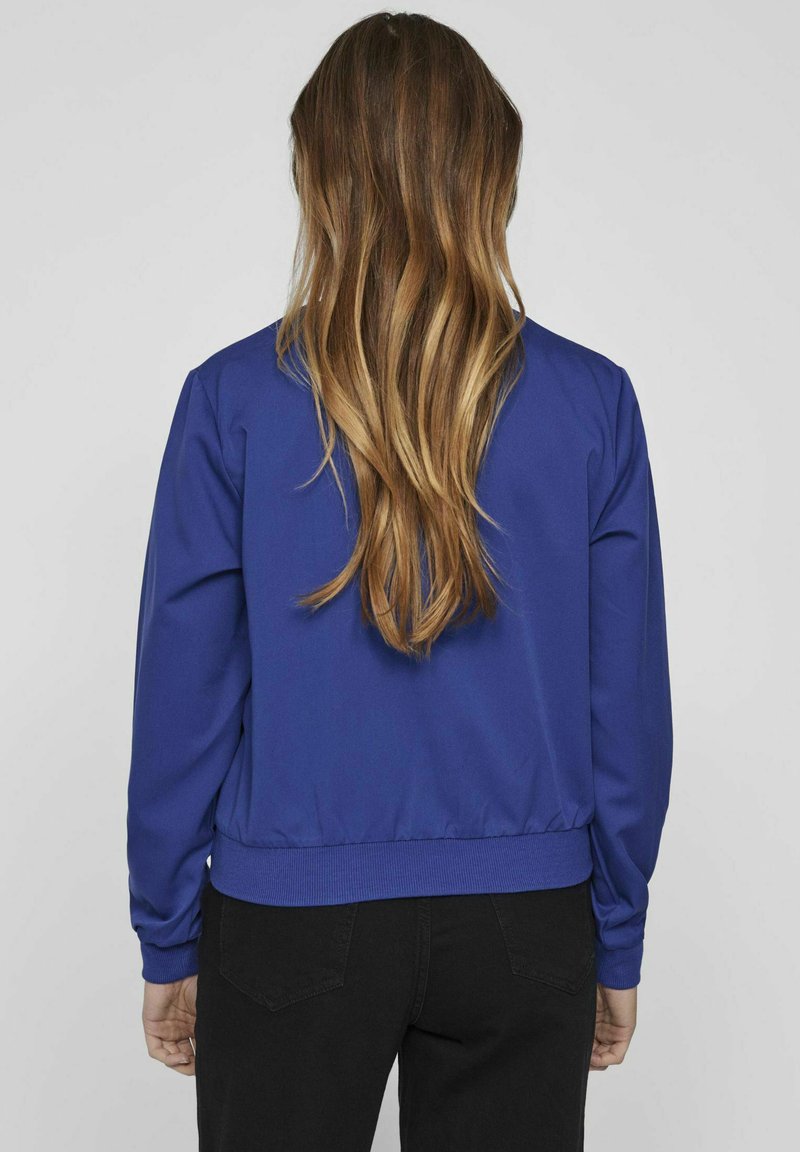 Niebieska bomberka z prążkowanym kołnierzem i mankietami, charakteryzująca się gładką fakturą oraz elastycznym pasem. Widok z tyłu, podkreślający design.