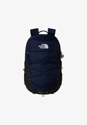 Zaino blu navy con dettagli neri, cordino elastico sulla parte frontale, spallacci imbottiti regolabili e un anello di sospensione per un facile trasporto.