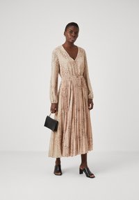 Μακρυμάνικο φόρεμα με V-λαιμόκοψη σε ανοιχτό μπεζ, με λεοπάρ σχέδιο, πλισέ φούστα, ελαστική μέση και μαύρες αξεσουάρ. Λείο υλικό.