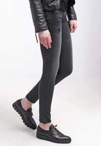Chaqueta de cuero negra, jeans ajustados grises con detalles desgastados y zapatos negros sin cordones con suela texturizada.