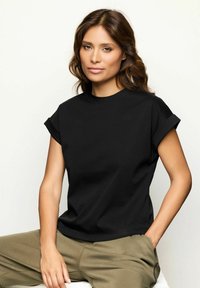 Sort bomulds t-shirt med korte, rullede ærmer, rund halsudskæring, afslappet pasform, parret med olivengrønne løse bukser. Minimalistisk design.