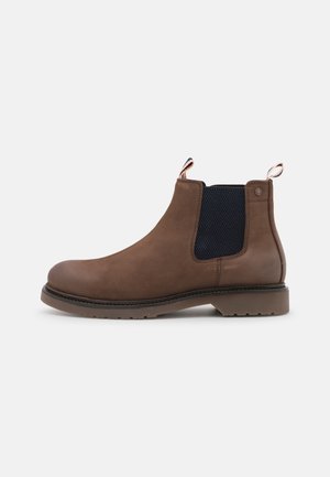Bota Chelsea de cuero marrón con paneles laterales elásticos, puntera redondeada y suela de goma. Presenta hebillas para facilitar su uso.