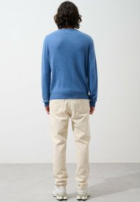 Blauer Rundhalsausschnitt-Pullover aus weichem Stoff, kombiniert mit hellbeigen Hosen und Laufschuhen; von hinten aufgenommen.
