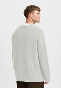 Light gray, ribbed knit sweater with a crew neck and drop shoulders, featuring a relaxed fit and a slightly longer back hem.